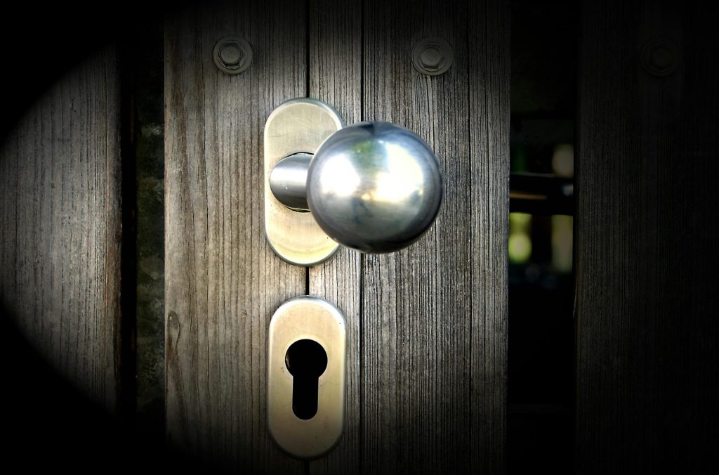 Gros plan sur une poignée de porte métallique et une serrure sur un portail en bois, mettant l'accent sur la sécurité et le design.