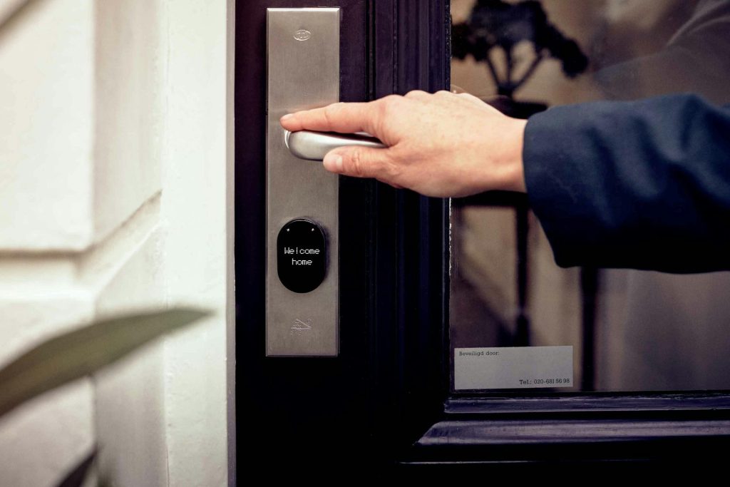 Une main ouvrant la porte d'une maison intelligente dotée d'un panneau d'accès numérique, symbole de sécurité et de technologie.